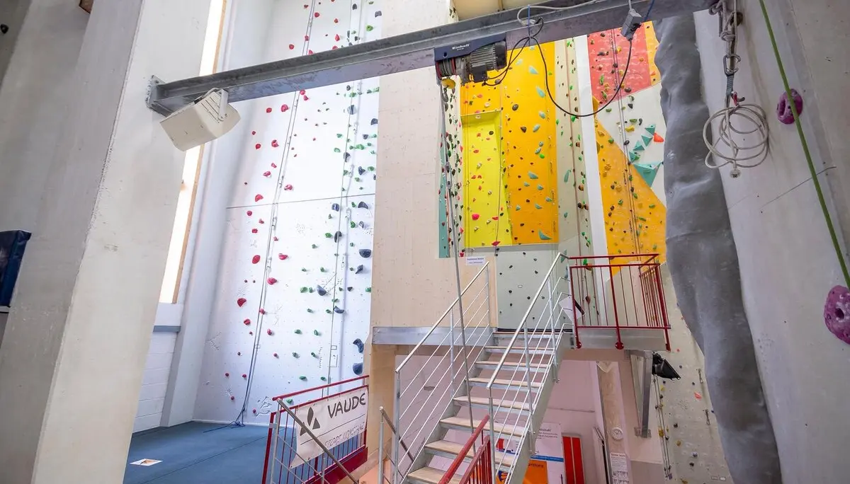 Innenansicht einer modernen Kletterhalle mit bunten Kletterwänden und verschiedenen Routen, zugänglich über eine Treppe. | © DAV Konstanz, Michael Dörfer