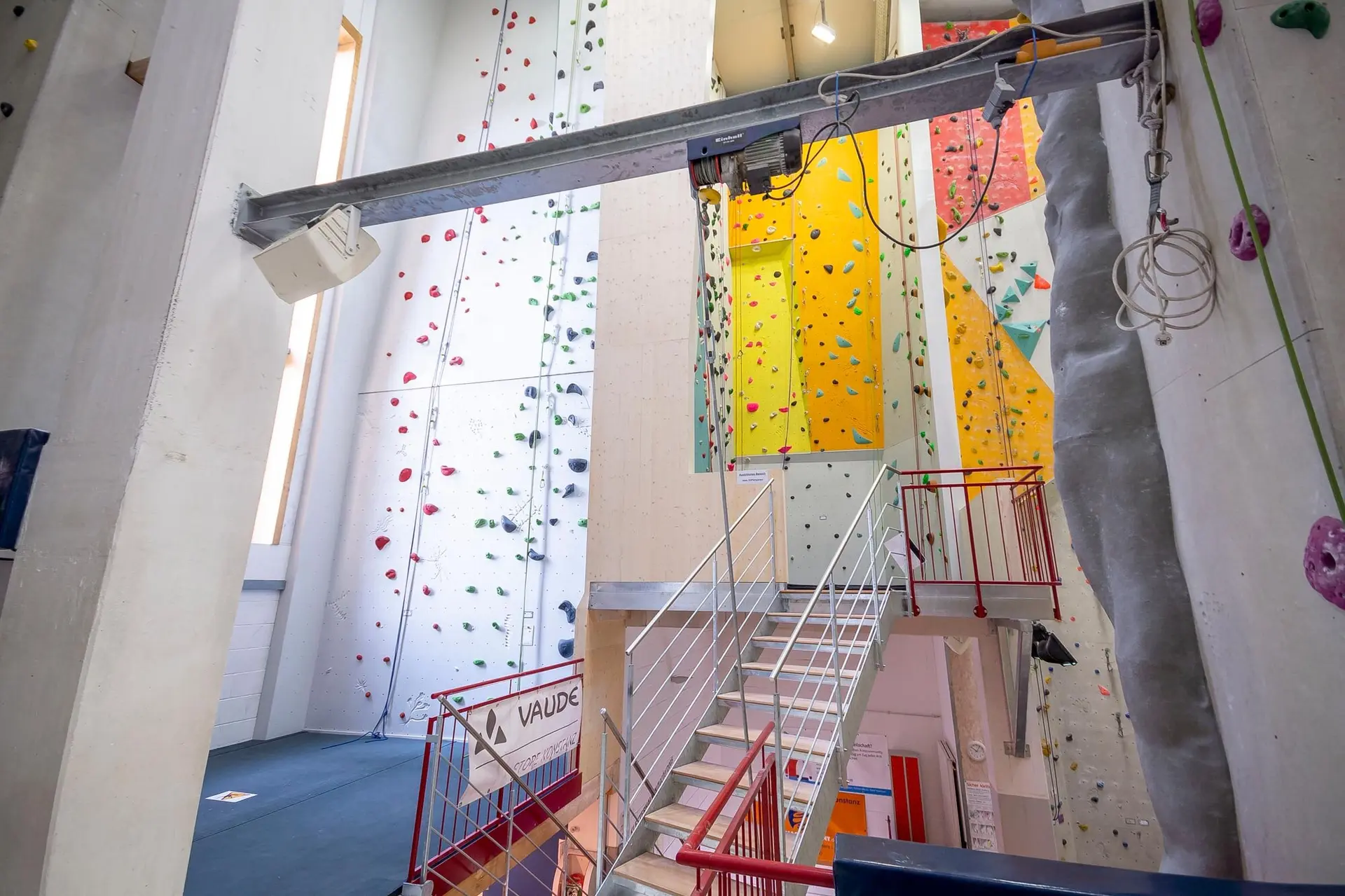 Innenansicht einer modernen Kletterhalle mit bunten Kletterwänden und verschiedenen Routen, zugänglich über eine Treppe. | © DAV Konstanz, Michael Dörfer