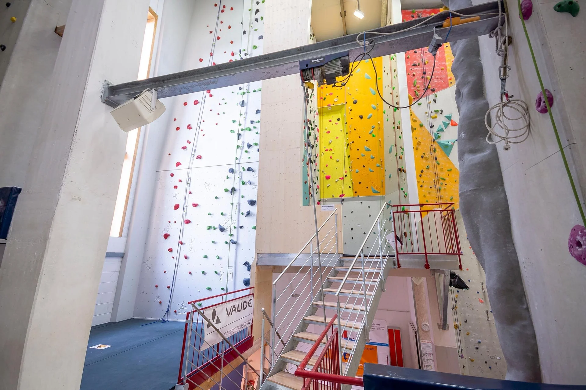 Innenansicht einer modernen Kletterhalle mit bunten Kletterwänden und verschiedenen Routen, zugänglich über eine Treppe. | © DAV Konstanz, Michael Dörfer