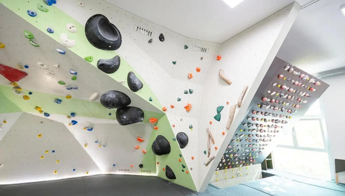 Helle Indoor-Boulderhalle mit geometrisch gestalteten Wänden, vielen bunten Klettergriffen und großen schwarzen Volumen, weicher Boden mit Matten. | © DAV Konstanz, Michael Dörfer