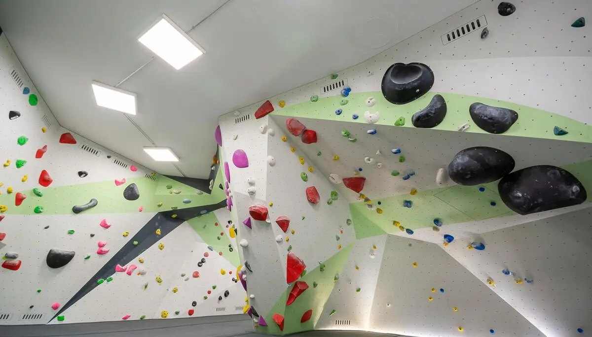 Helle Indoor-Boulderhalle mit geometrisch gestalteten Wänden, vielen bunten Klettergriffen und großen schwarzen Volumen, weicher Boden mit Matten. | © DAV Konstanz, Michael Dörfer