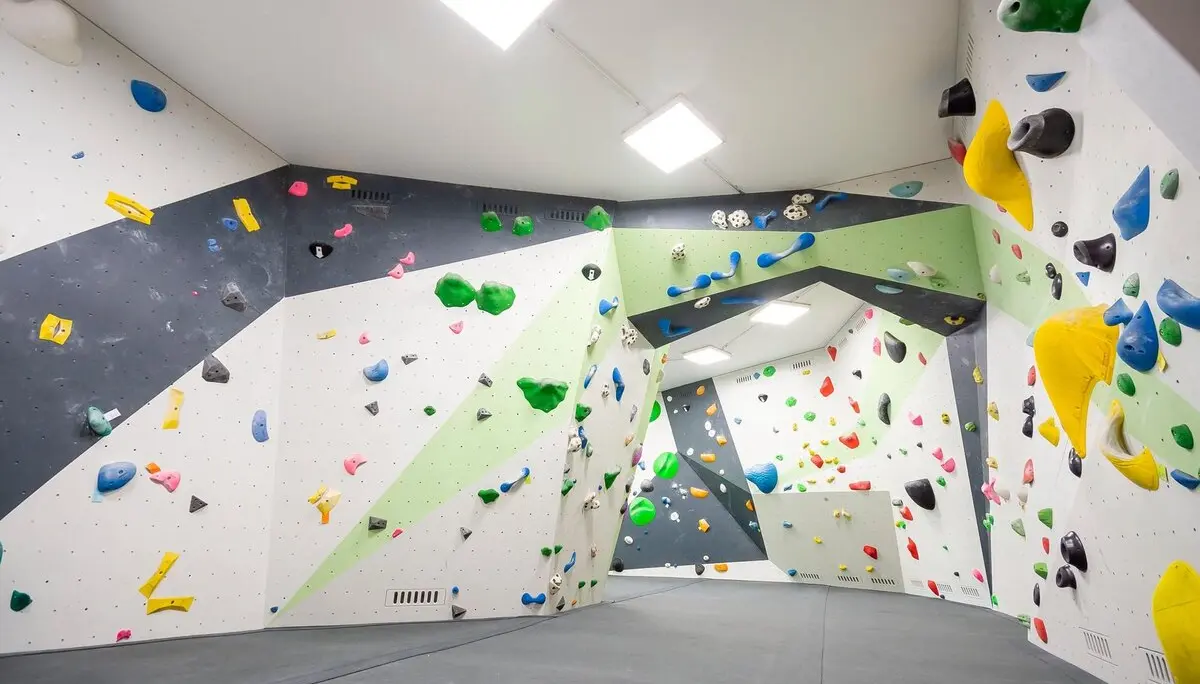 Helle Indoor-Boulderhalle mit geometrisch gestalteten Wänden, vielen bunten Klettergriffen und verschiedenen Volumen, weicher Boden mit Matten. | © DAV Konstanz, Michael Dörfer