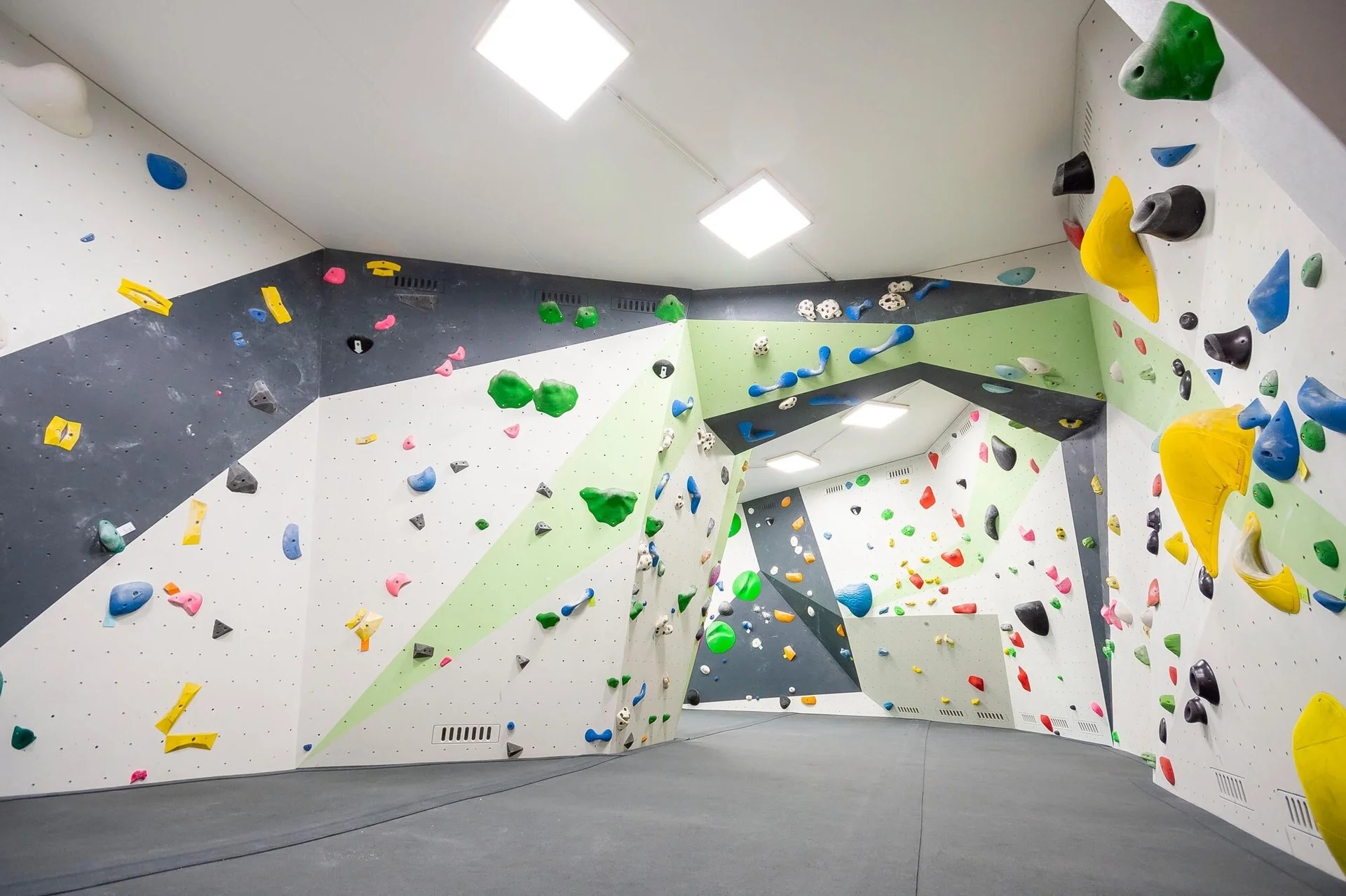 Helle Indoor-Boulderhalle mit geometrisch gestalteten Wänden, vielen bunten Klettergriffen und verschiedenen Volumen, weicher Boden mit Matten. | © DAV Konstanz, Michael Dörfer